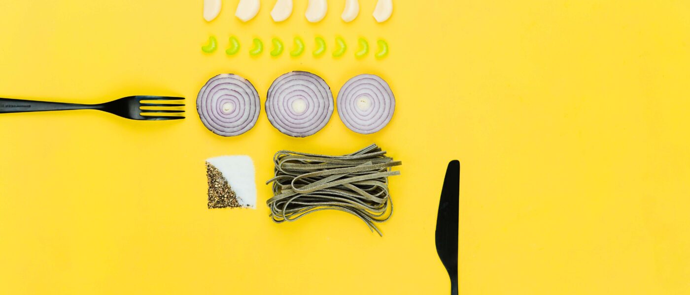 Plato con una pequeña porción de pasta, cubiertos y medicación sobre un fondo amarillo.