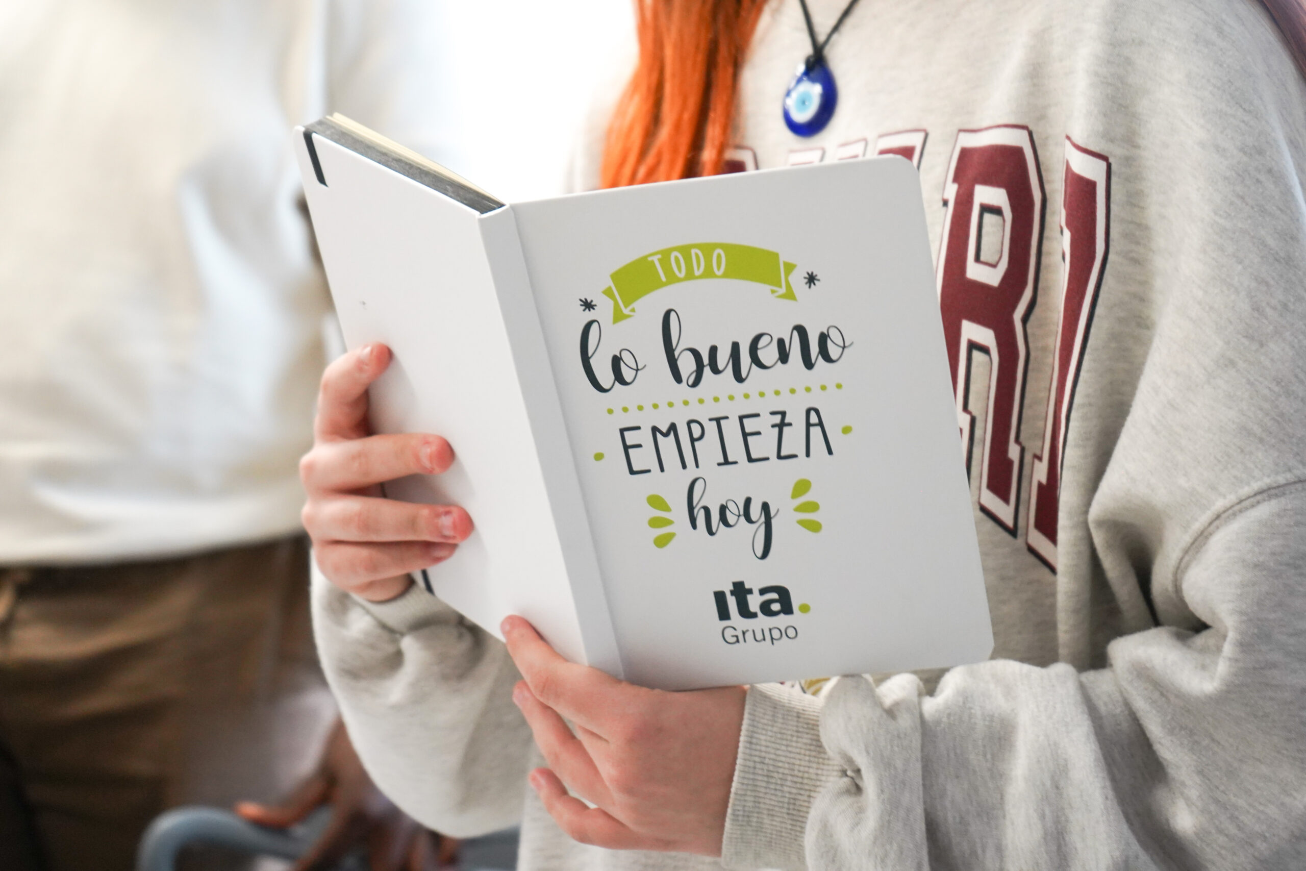 Joven sosteniendo libro con un mensaje optimista "lo bueno empieza hoy"