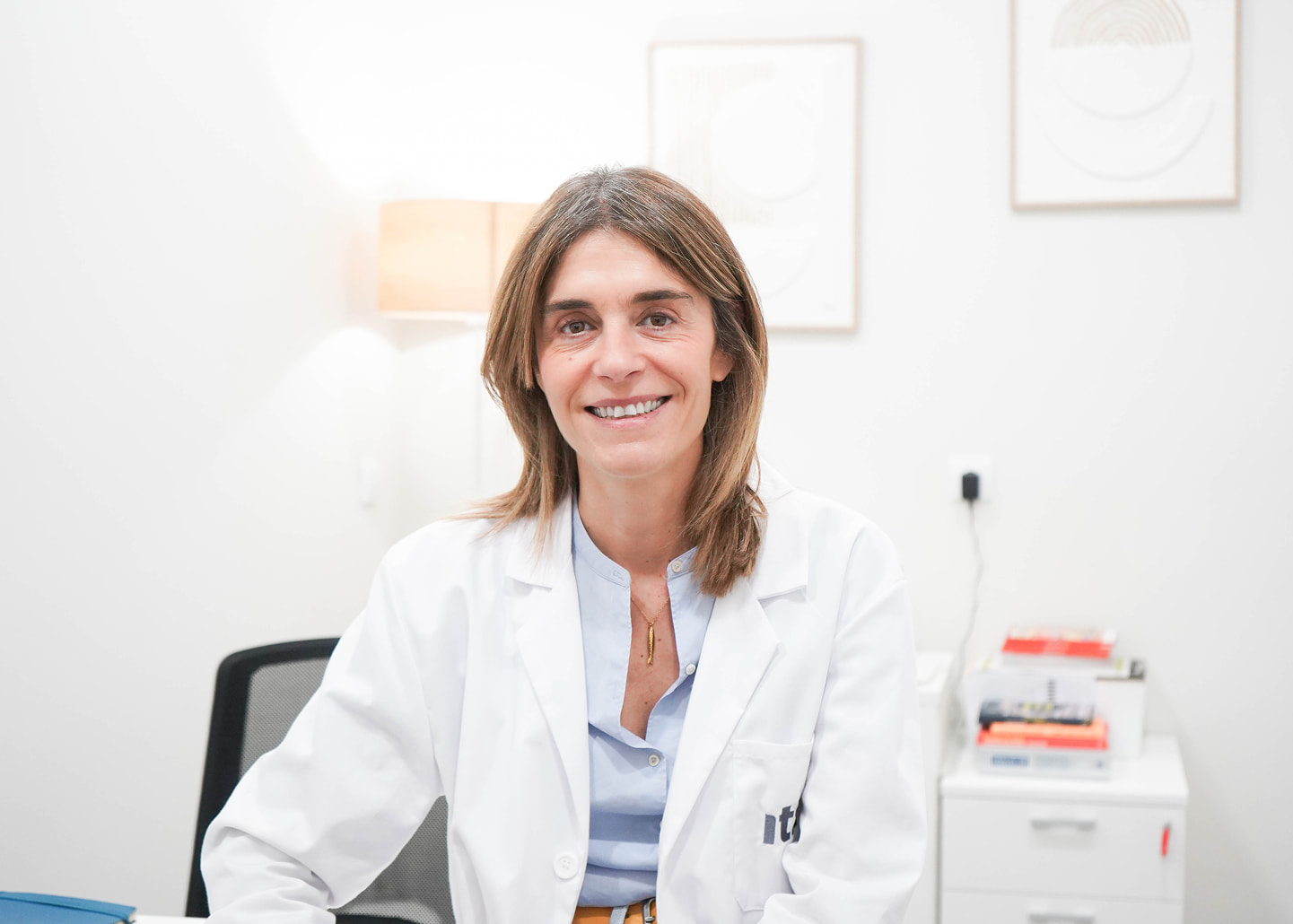 Profesional en bata sonriendo a cámara desde su despacho