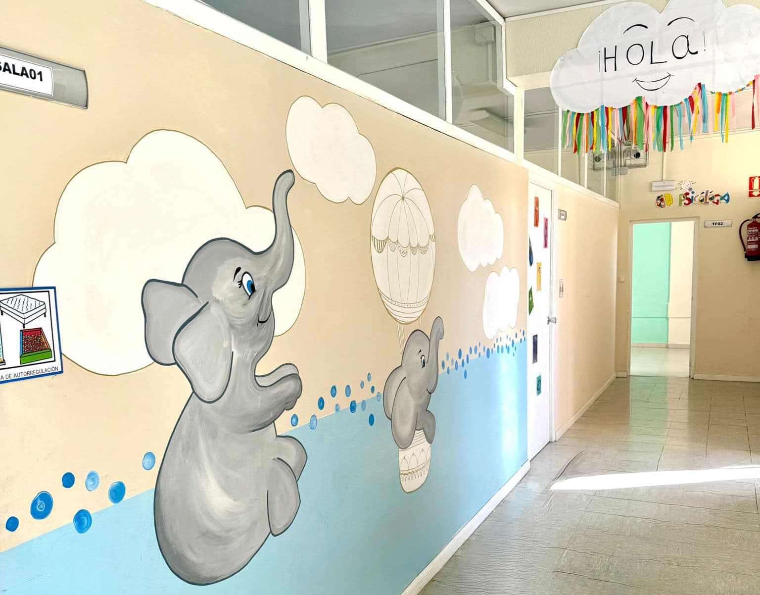 Pasillo de un centro infantil con mural de animales y nubes en la pared
