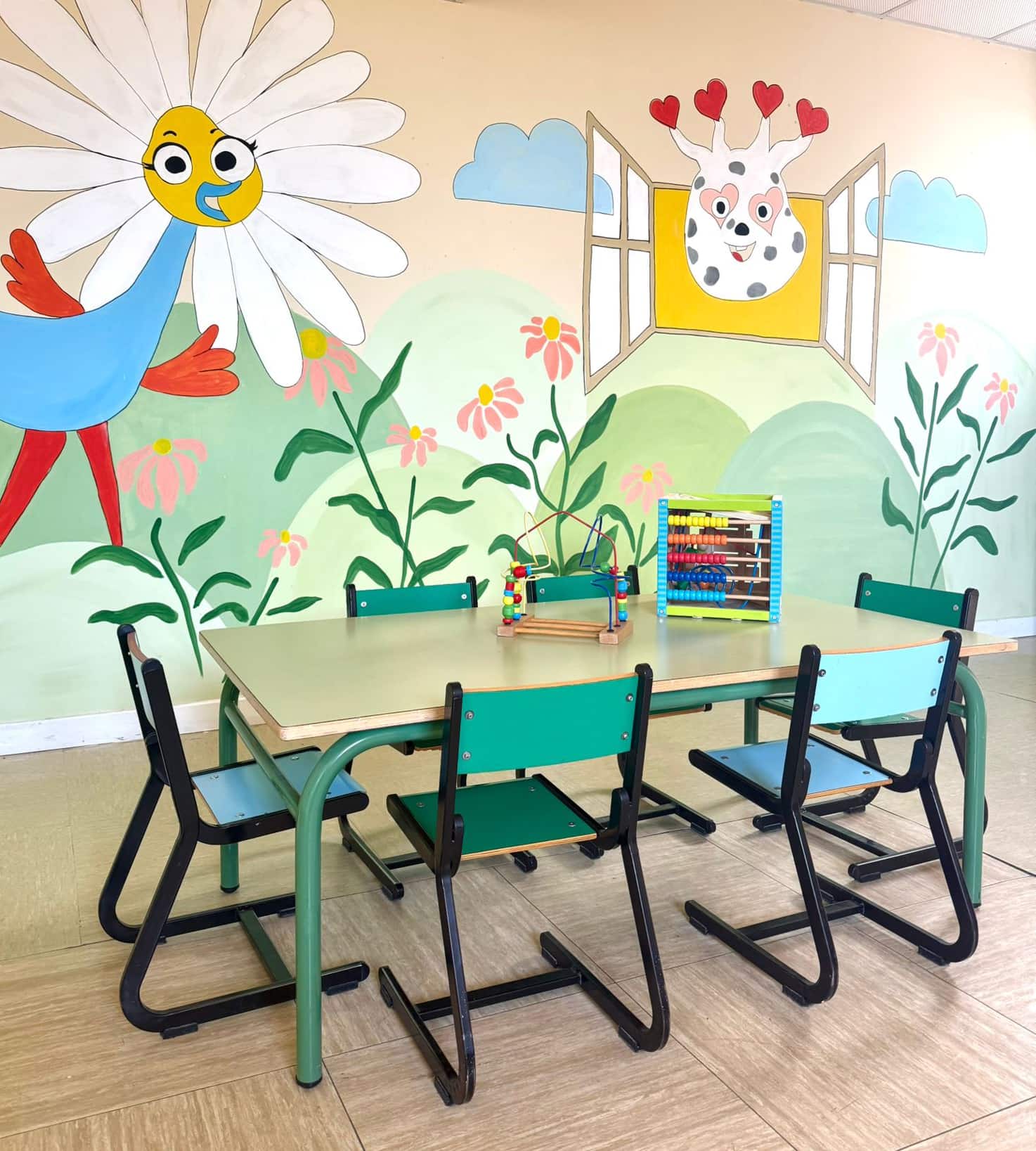 Aula infantil con mesas y sillas frente a un mural colorido de flores y personajes sonrientes