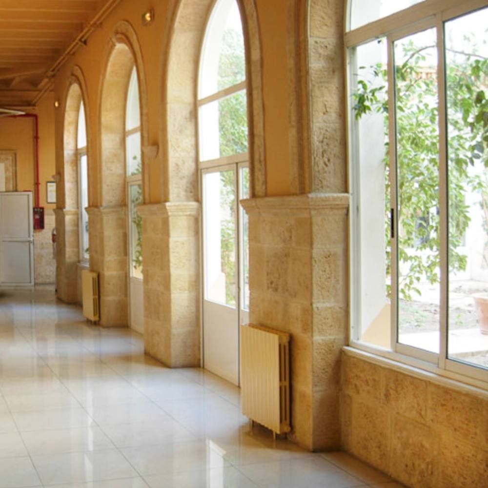 Pasillo interior de un edificio histórico con arcos de piedra y grandes ventanales