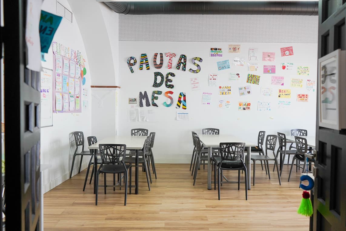 Sala de actividades de Ita Sevilla con mesas, sillas y mural
