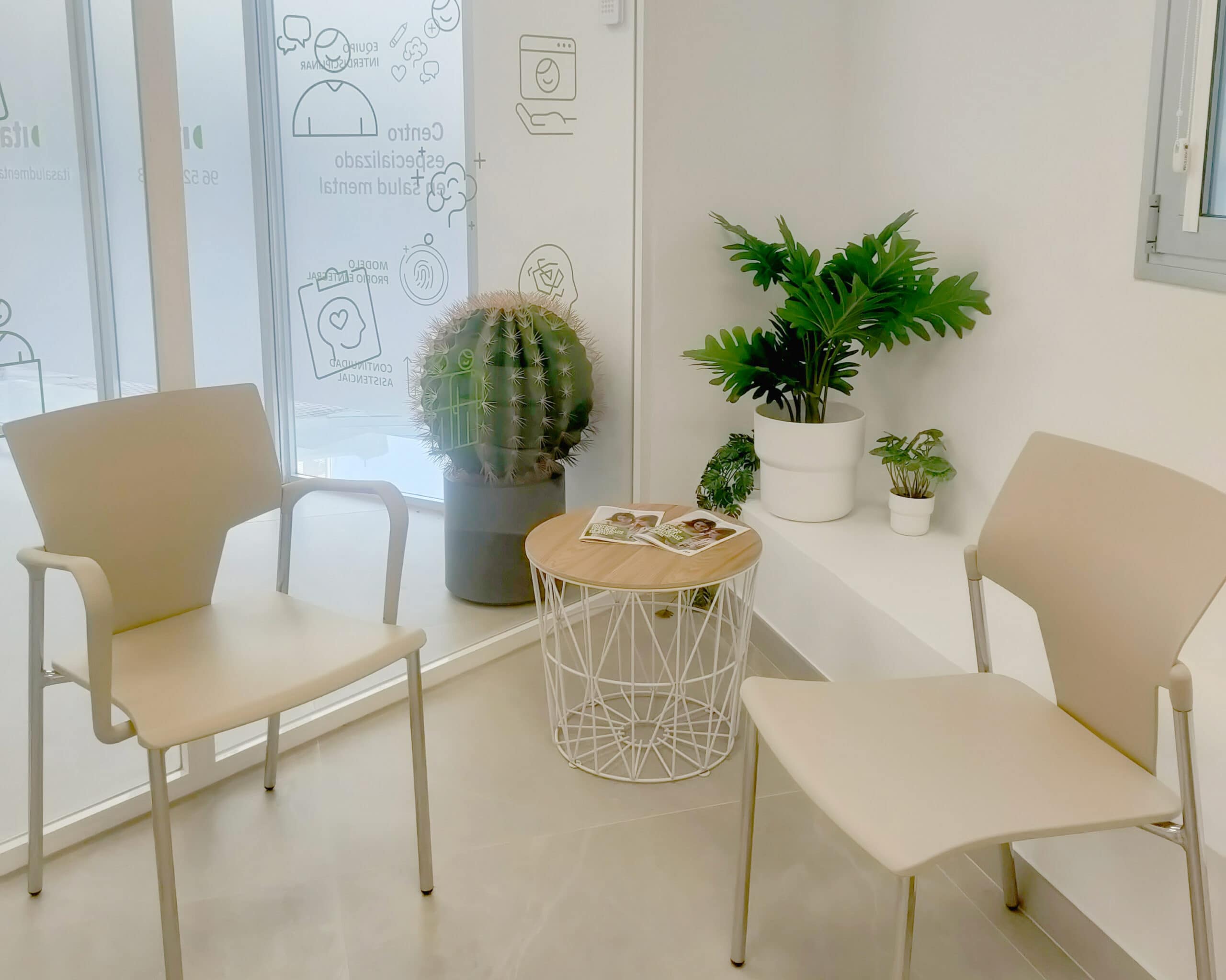 Zona de descanso compuesta por una mesa, dos sillas beige y una planta